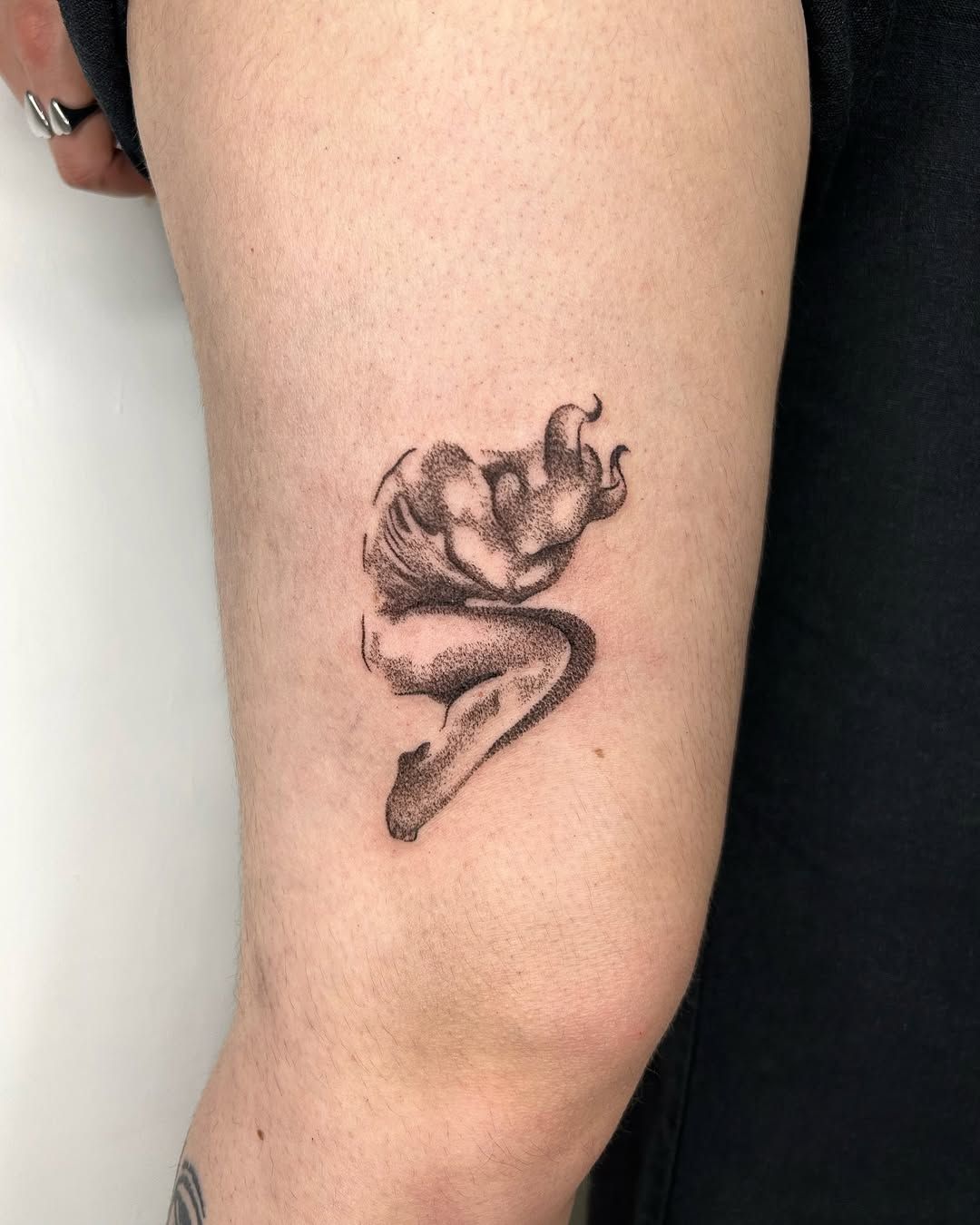 Figure repliée prolongée de flammes, tatouée sur un bras.