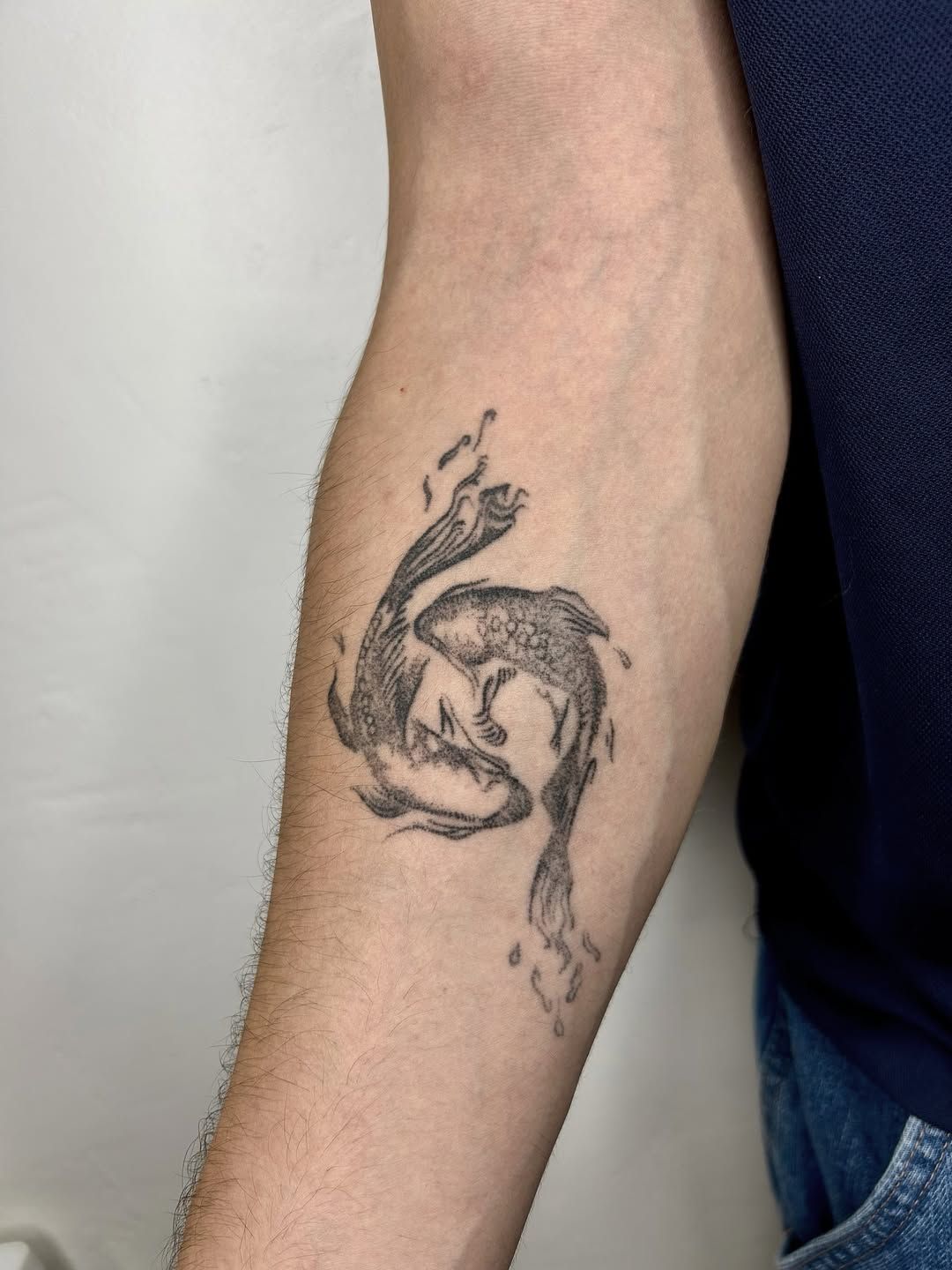 Deux poissons en mouvement, tatoués en noir sur un avant-bras.
