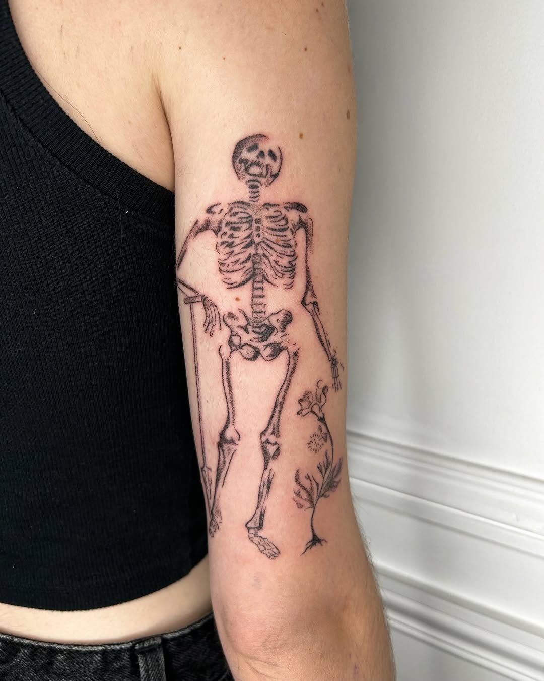 Squelette et fleurs tatoués en pointillé sur le haut du bras.